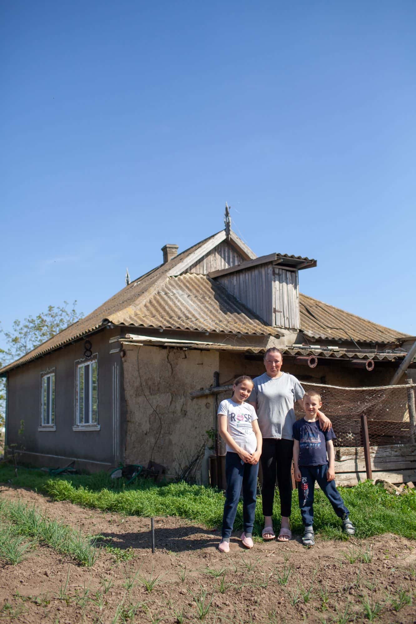 En mor og to barn smiler foran huset sitt på landsbygda